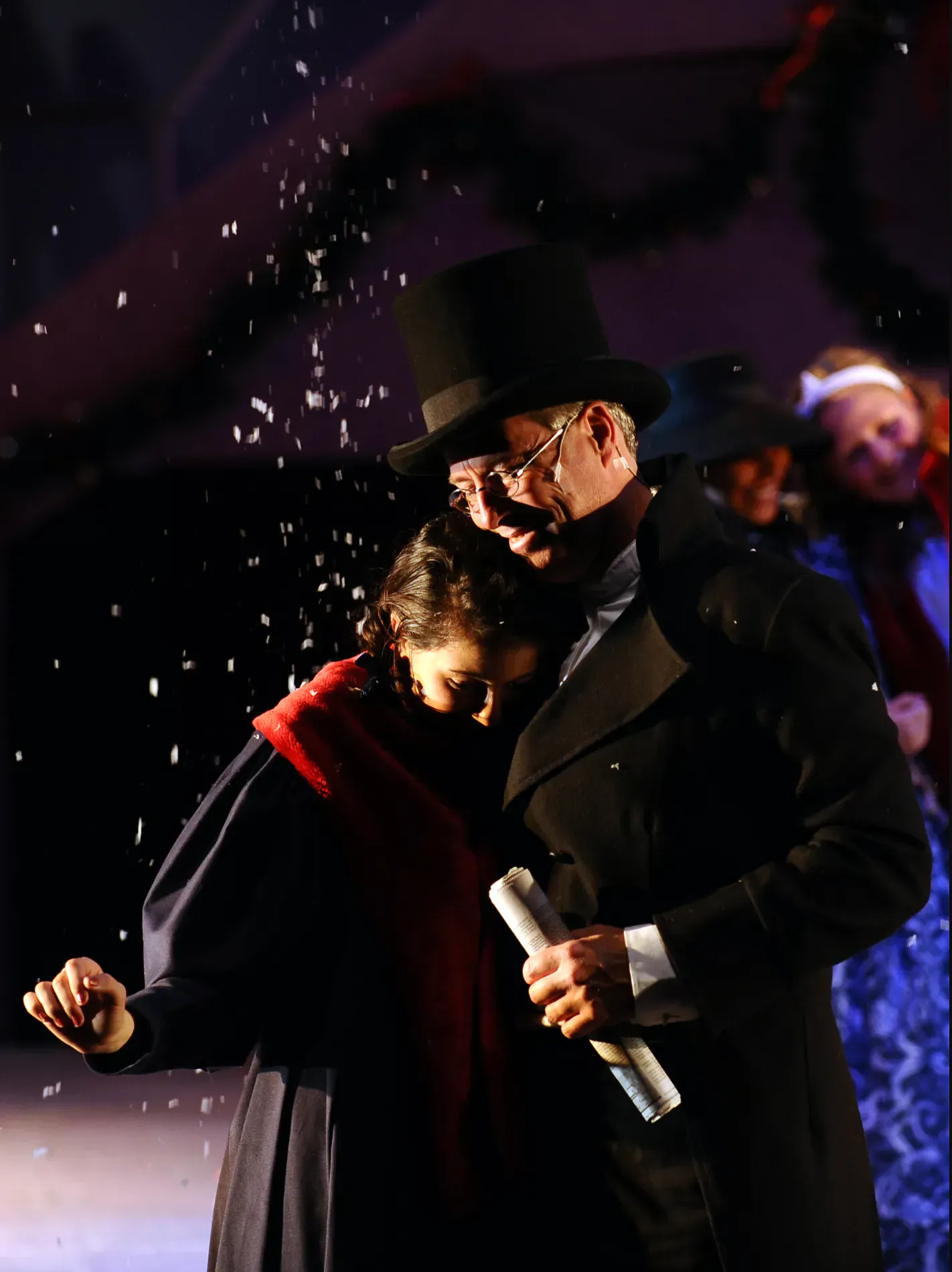 A young performer embraces an older man in a top hat during the snow scene in A Little Princess.