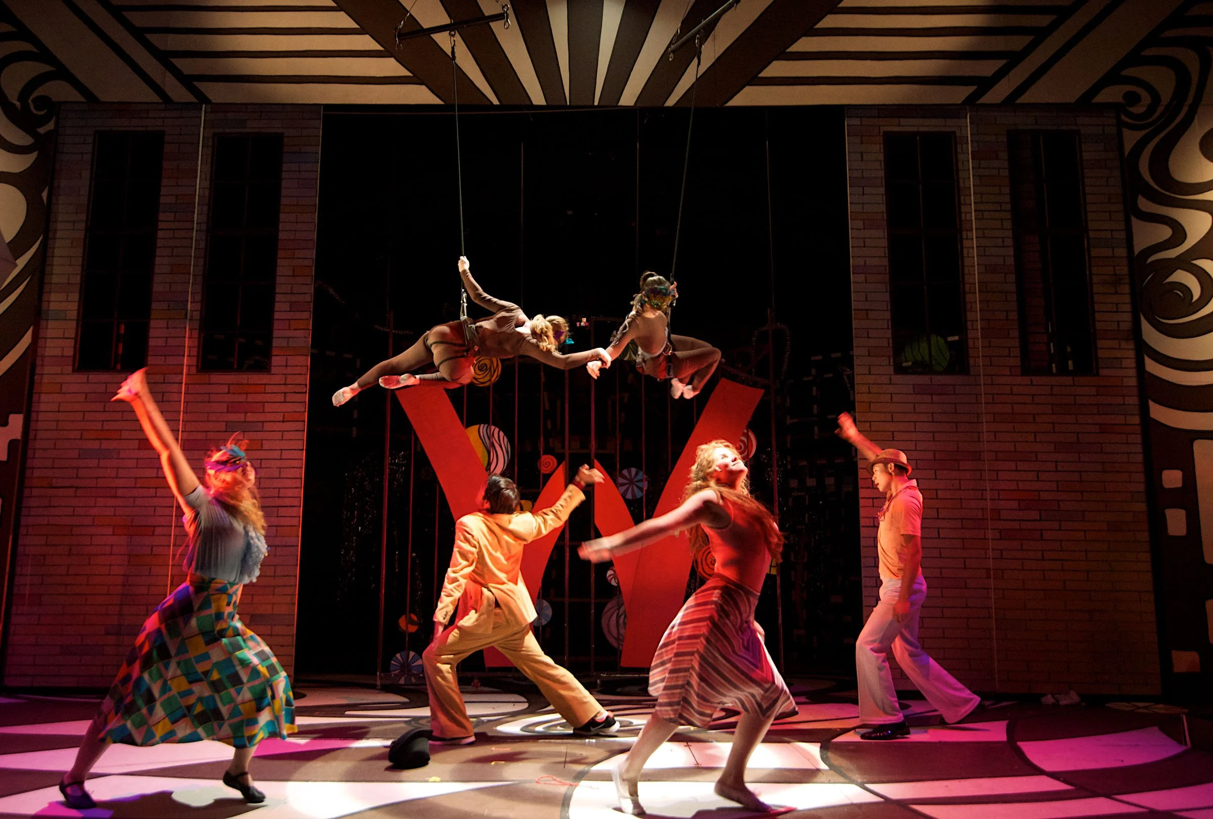 The cast of Willy Wonka performing beneath aerialists.